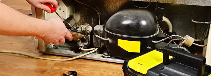 Refrigerator repair technician fixing the compressor and wiring in Auburn, NH