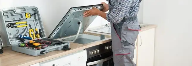 Cooktop repair technician lifting a built-in stovetop for service in Manchester, NH