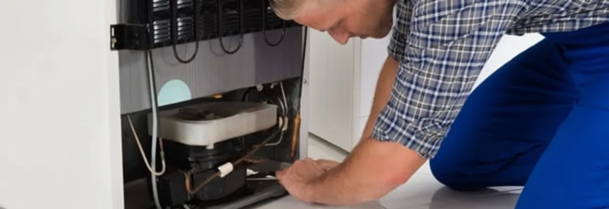 Refrigerator repair technician servicing the compressor and condenser area in Manchester, NH