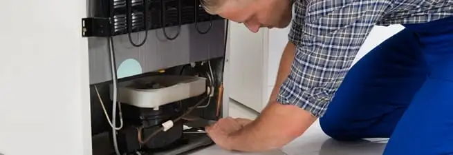 Refrigerator repair technician servicing the compressor and condenser area in Manchester, NH