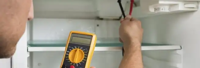 Refrigerator repair technician testing electrical components with a multimeter in Manchester, NH