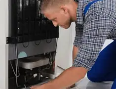 Refrigerator repair technician servicing the compressor and condenser area in Manchester, NH
